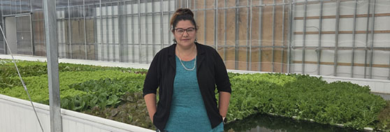 Mindy Knott stands among the bountiful crops at her community’s aquaponics greenhouse