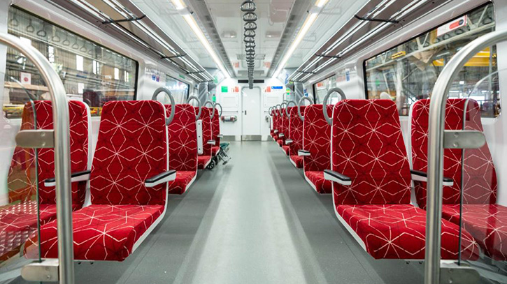 Interior of a transit vehicle with red patterned seats, central aisle, and large windows.